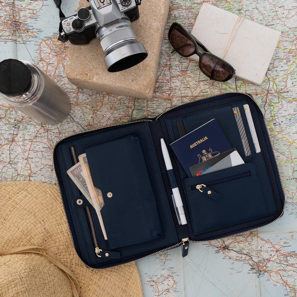 An opened navy pebbled leather travel wallet sitting on a world map, a camera, straw hat and sunglasses
